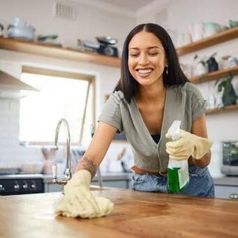 Woman cleaning a wooden countertop with a cloth and spray bottle.