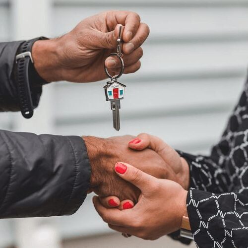 A person handing over a house key during a handshake.