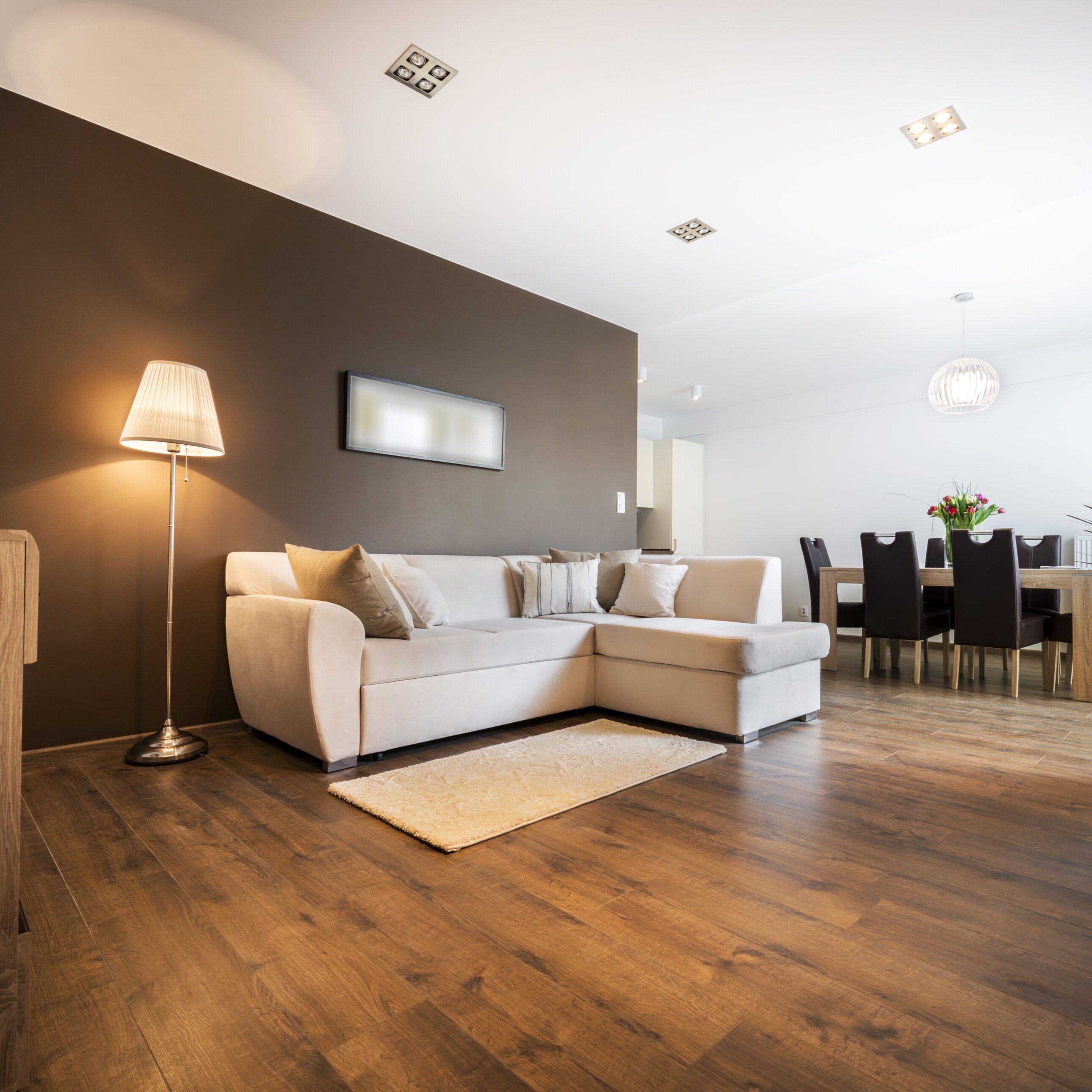 Modern living room with beige sectional sofa and wooden flooring.